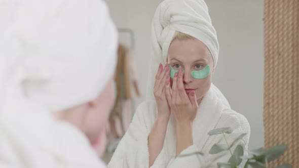 Happy Attractive Woman in Bath Towel With Cosmetic Patches Under Eyes Kooking at Mirror and Enjoying alt