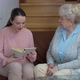Young Positive Beautiful Woman Reading Book for Senior Lady Discussing Story and Smiling