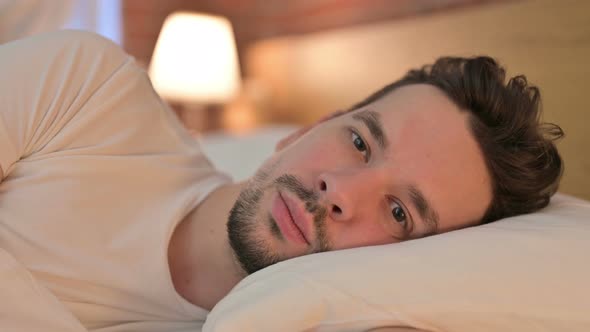 Portrait of Young Man Looking at Camera in Bed alt