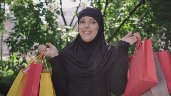 Cheerful Young Muslim Woman Raising Hands with Shopping Bags and Smiling at Camera. Portrait alt