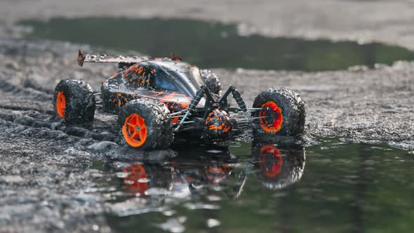 Dirty, orange RC-Car got stuck in the mud on a wet forest mire path. 4KHD alt