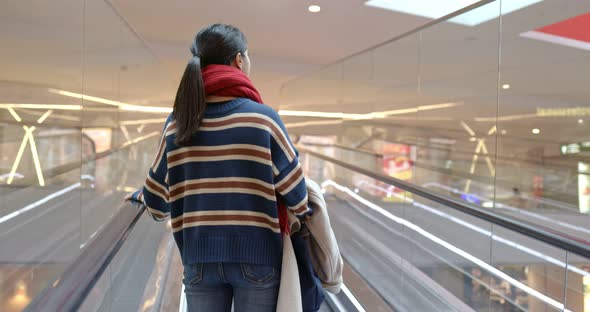 Woman taking escalator inside shopping mall
