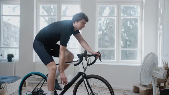 Cyclist Training on an Exercise Bike and Drinking Water Staying at Home