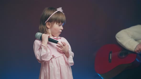 Cute Little Girl in a Pink Vintage Dress Stands with a Microphone on Stage