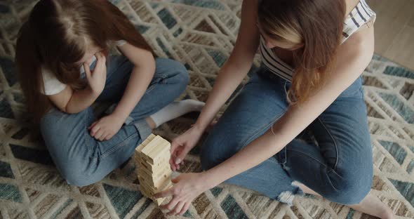 Mother and Daughter Build Tower From Wooden Bricks Sitting on a Floor at Home alt
