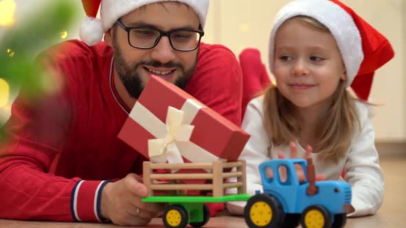 Father Gives Child Gift Next to Christmas Tree