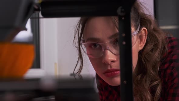 Young Woman with Protective Eyeglasses Using 3D Printer alt