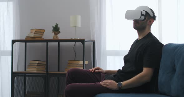 Man is Watching Cinema at Home Using Modern Headmounted Display Sitting on Couch in Living Room alt