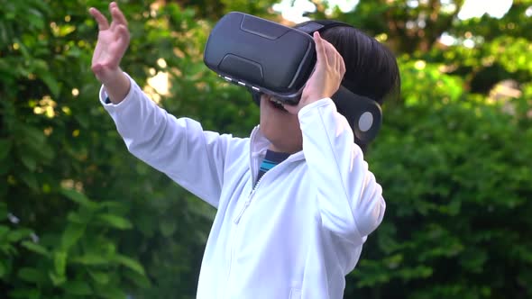 Asian Child With Virtual Reality Headset Touching Outdoors alt