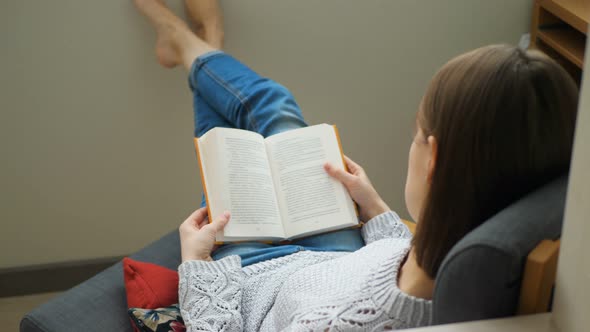 Young Woman Relaxing in Her Chair and Flipping Through the Book She Wants To Read