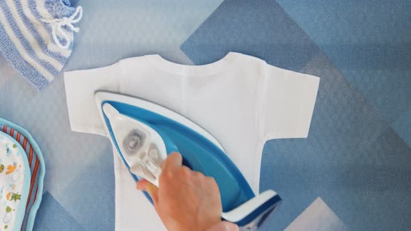 Motherhood. Female Hands Ironing Clothes with Iron on Ironing Board