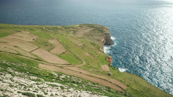 AERIAL: Greenery Plains of Ta Cenc Cliffs near Blue Mediterranean Sea on Windy Day