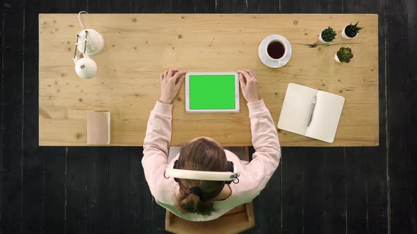 Girl Listening To the Music From a Tablet Sitting at the Desk. Green Screen Mock-up Display alt