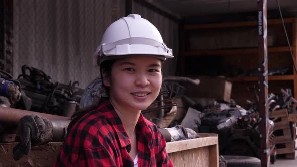 Asian female worker putting on white safety hard hat, and looking at the camera