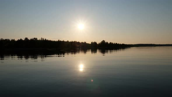 Bright sun moving down, dark trees on shore, look from calm water of Ladoga lake