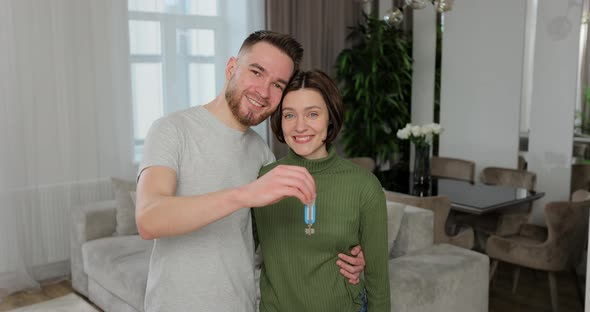 Happy Young Family Couple Looking at Camera Showing Keys Form New Apartment alt