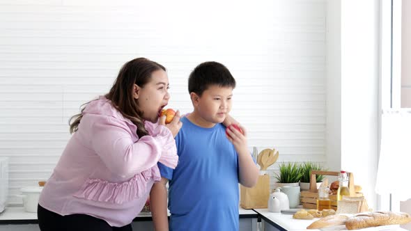 Happy Young mother and son eating apple in the kitchen
