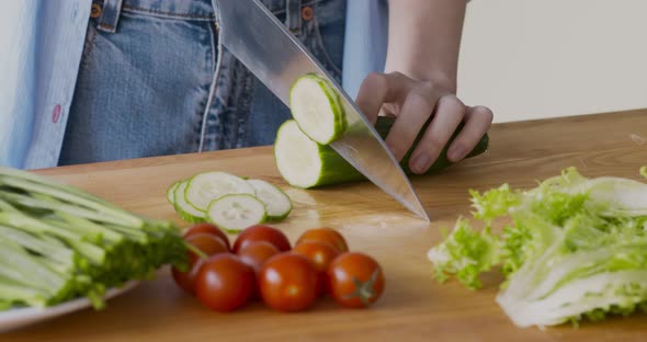 Woman Cutting Fresh Cucumber for Vegetable Salad at Kitchen alt