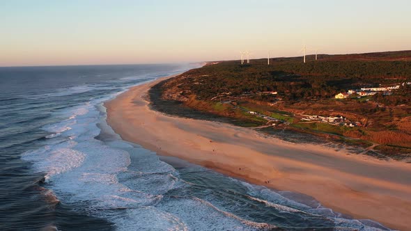 Praia do Norte Beach in Nazare Portugal with string waves and wind turbines in the distance, Aerial alt