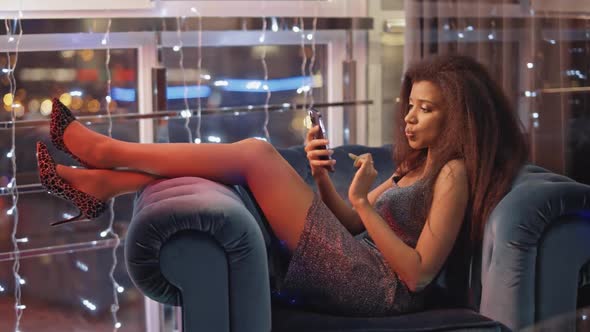 Glamorous African Female Lies on a Chair in Lounge Area and Use Smartphone Online Communication Girl alt