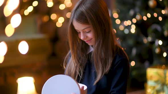 Happy girl unwrapping christmas present looking in box. alt