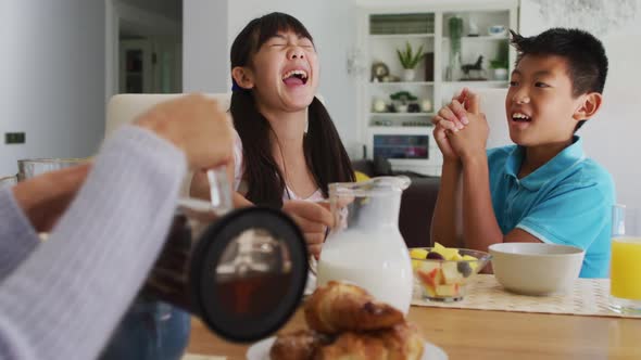 Happy asian brother and sister in kitchen having breakfast and laughing with parents alt