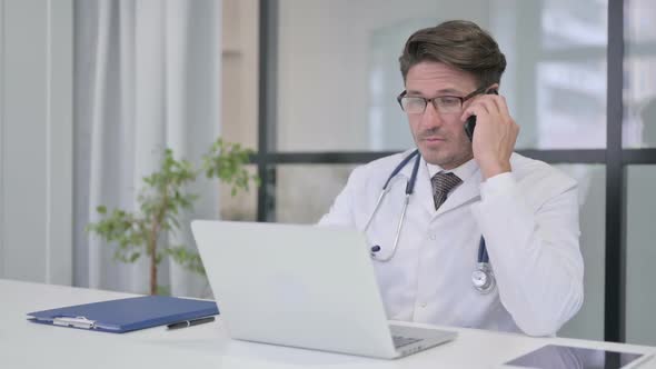 Doctor Talking on Phone while Working on Laptop alt