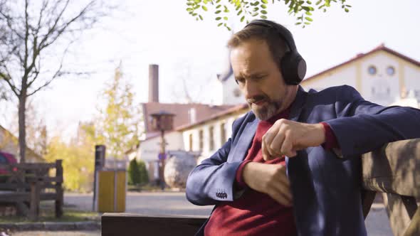 A Middleaged Handsome Caucasian Man Listens to Music with Headphones and Scrolls on a Smartphone