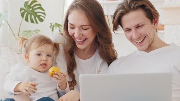 Portrait Young Caucasian Parents with Little Daughter Sitting on Couch at Home Using Laptop for alt