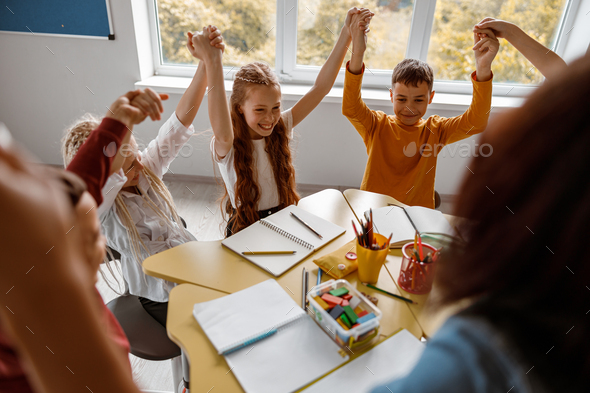 Schoolchildren sitting at the table and raising their hands up Stock ...