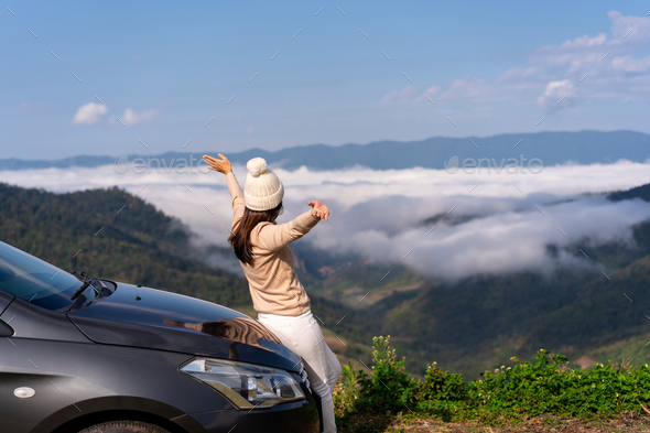 Young woman travelers with car watching a beautiful sea of fog over the mountain while traveling