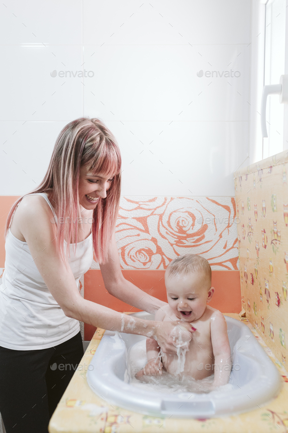 portrait of a baby is being bathed by his mother using tub at home
