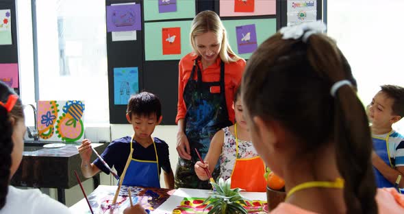 Teacher assisting schoolkids in drawing class alt