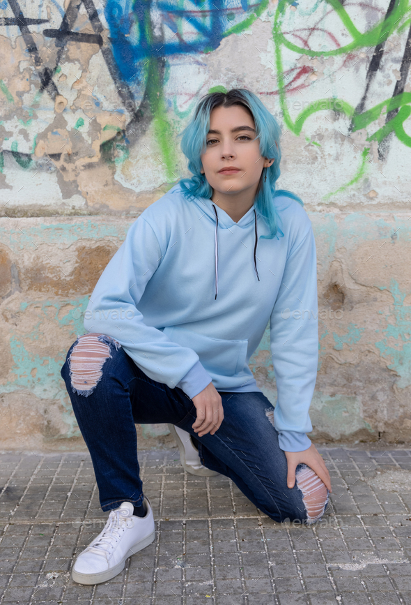 Blue haired Teenage girl in blue hoodie staying near graffiti wall with red water  bottle Stock Photo by katrinshine