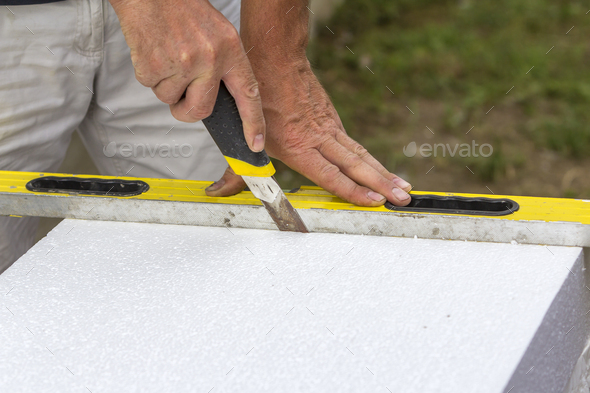 Close-up of worker hand with knife and level cutting white rigid polyurethane foam sheet for house