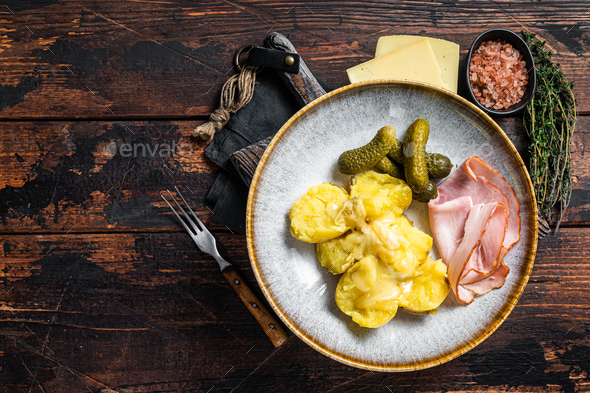 Melted Raclette Swiss cheese with boiled potato and ham. Wooden background. Top view. Copy space