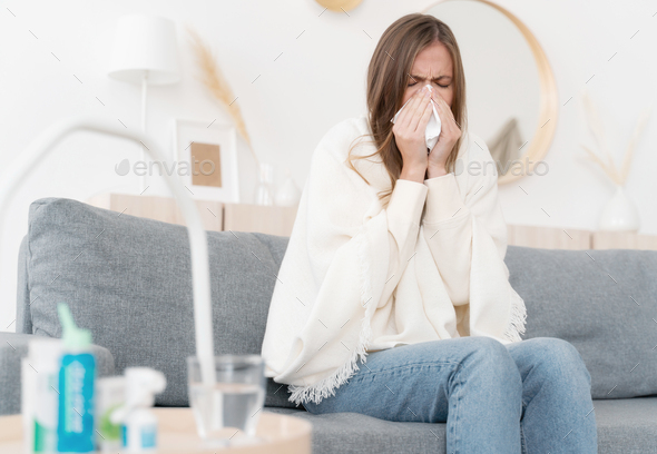 Sick young woman blowing nose, coughing or sneezing in tissue, suffering from flu