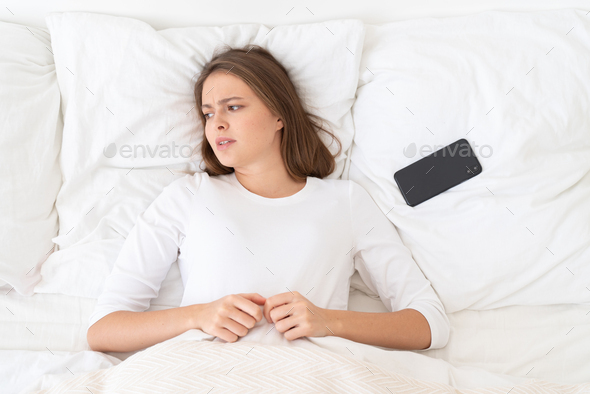 Young female put away her smartphone after breakup with lover, lying in bed in morning
