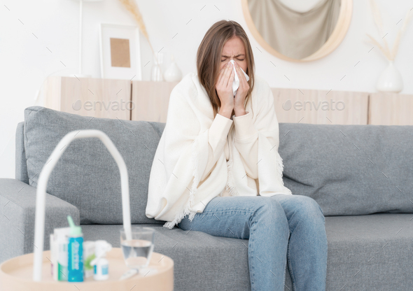 Ill young woman blowing nose, coughing or sneezing in tissue