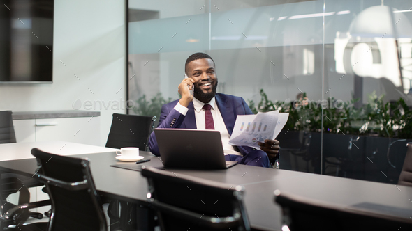 Smiling black boss having phone conversation at office, holding documents