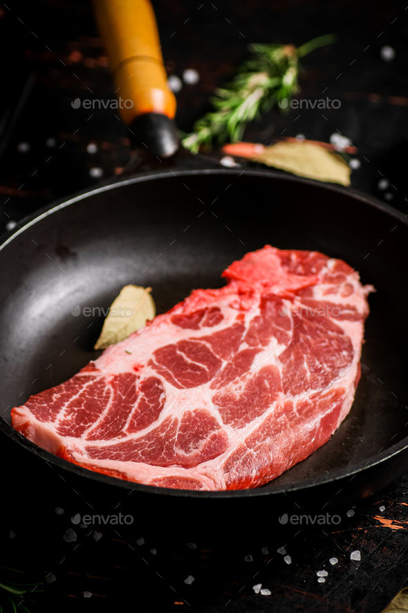 Raw pork steak in a frying pan with bay leaves and rosemary. Stock Photo by Artem_ka2