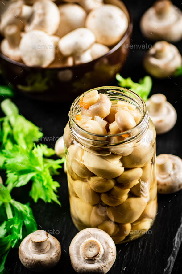 Pickled mushrooms in a jar with greens on a stone board. Stock Photo by