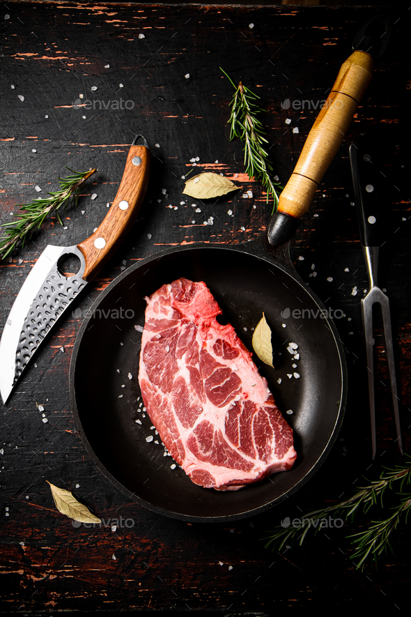 Raw pork steak in a frying pan with bay leaves and rosemary. Stock Photo by Artem_ka2