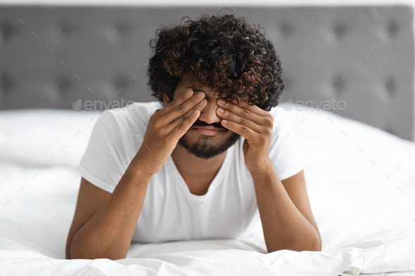 Upset guy laying on bed, rubbing his eyes