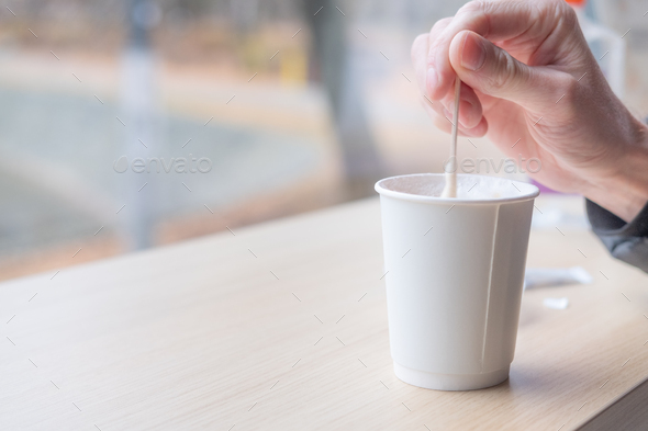 stirring sugar in a glass. Coffee to go. Coffee in a paper cup. Hand holding a spoon