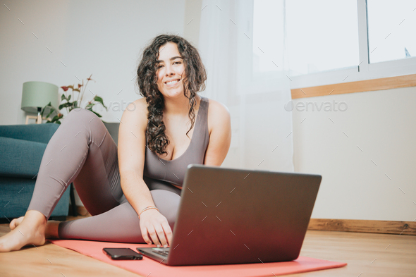 Young plus size woman sitting on the floor resting after doing a online yoga class with his laptop