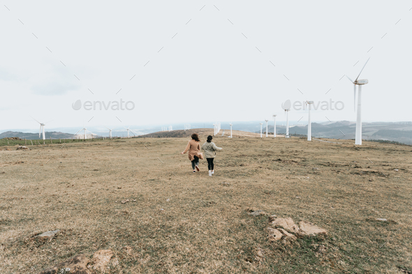 Vintage cinematic image of two young woman running between electrical wind mills with soft tones