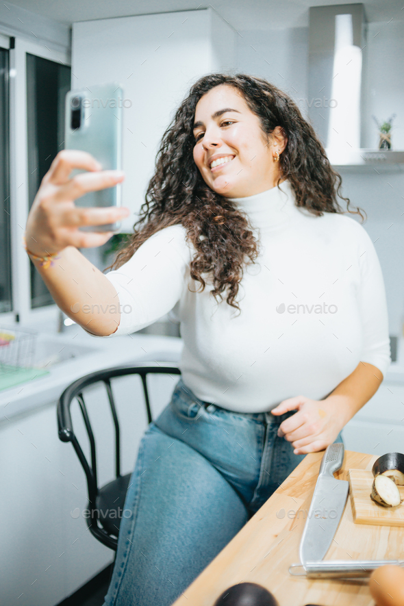 Young plus size spanish woman blogging about his diet and eating habits at a modern kitchen