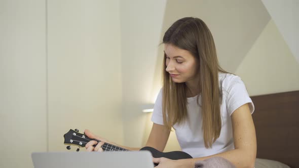 Young Woman Practicing and Learning How To Play Ukulele on Laptop Computer Monitor, Watching Online