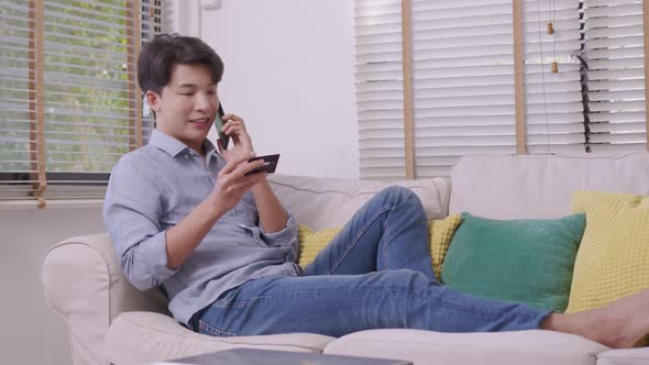 Asian man makes a payment via the internet. On the sofa at home alt